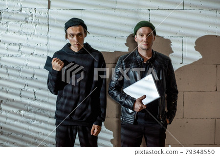 Two young male hackers standing by wall Two young male hackers standing by wall 79348550