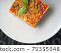 Piece of lasagna with a basil leaf on white plate 79355648