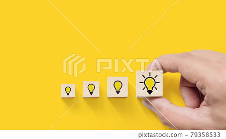 Hand picked wooden cube block with light bulb icon on yellow background 79358533