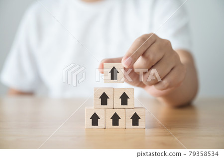 Business growth success concept. Hand picked wood cube block with arrow on top pyramid Business growth success concept. Hand picked wood cube block with arrow on top pyramid 79358534