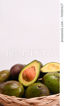 Whole and half avocado in a weaved basket. 79360427
