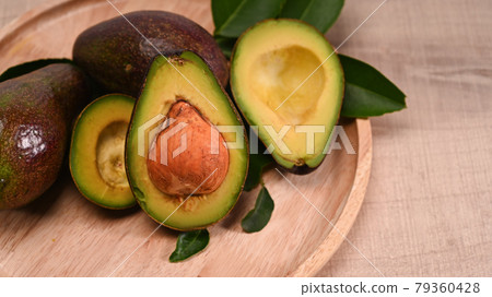 Close up whole avocado and half with seed on wooden plate. Close up whole avocado and half with seed on wooden plate. 79360428