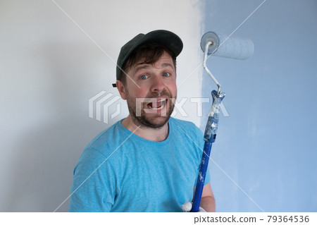 Young painter in blue t-shirt, cap and gloves painting a wall with paint roller. 79364536