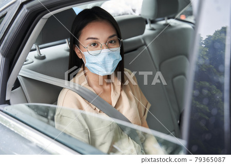 Businesswoman wearing protective mask is sitting on back seat of the car Businesswoman wearing protective mask is sitting on back seat of the car 79365087