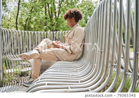 Boy sitting at the bench at the park and writing something at the notebook Boy sitting at the bench at the park and writing something at the notebook 79365348