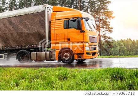 orange modern truck with a semi-trailer is driving on a wet road in the rain. Slippery road, tire grip, trucking industry orange modern truck with a semi-trailer is driving on a wet road in the rain. Slippery road, tire grip, trucking industry 79365718