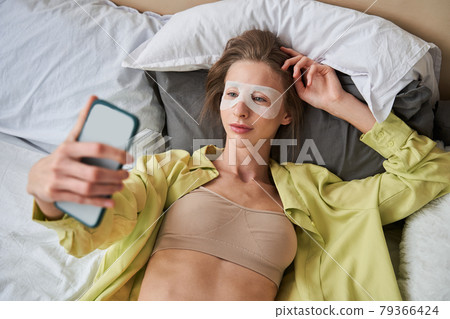 Woman wearing face mask smiling and looking at the smartphone while laying 79366424