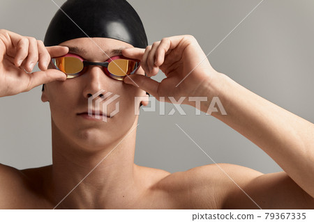 Swimmer in a cap and mask, on a gray background, preparing to swim, close-up, advertising banner for swimming pools, copy space Swimmer in a cap and mask, on a gray background, preparing to swim, close-up, advertising banner for swimming pools, copy space 79367335