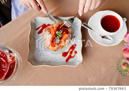 hands close-up. A woman eats a croissant with strawberries, mint and jam hands close-up. A woman eats a croissant with strawberries, mint and jam 79367663