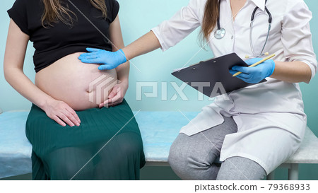 Doctor with clipboard examines pregnant patient on couch Doctor with clipboard examines pregnant patient on couch 79368933