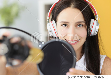 Portrait of smiling woman in headphones in front of microphone in studio Portrait of smiling woman in headphones in front of microphone in studio 79369288