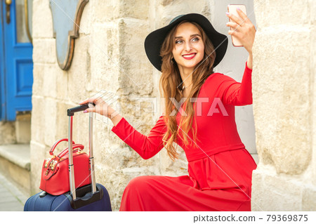 Beautiful young caucasian woman in black hat looking on the smartphone smiling and sitting on stairs at the door outdoors. Beautiful young caucasian woman in black hat looking on the smartphone smiling and sitting on stairs at the door outdoors. 79369875