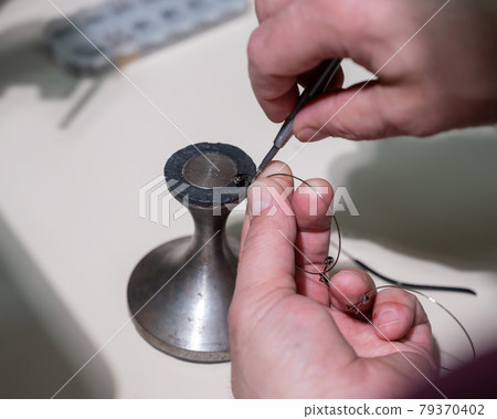 Optical technician fixing glasses. Close-up of male hands with screwdriver and goggles frame. 79370402