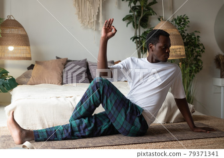 man doing yoga Spine twisting pose or ardha matsiendranasana sitting at the living room man doing yoga Spine twisting pose or ardha matsiendranasana sitting at the living room 79371341