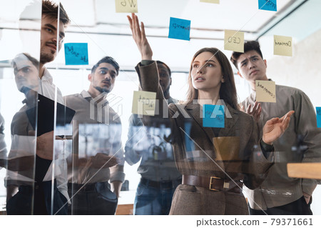 Colleagues brainstorming using sticky post-it notes on glass wall 79371661