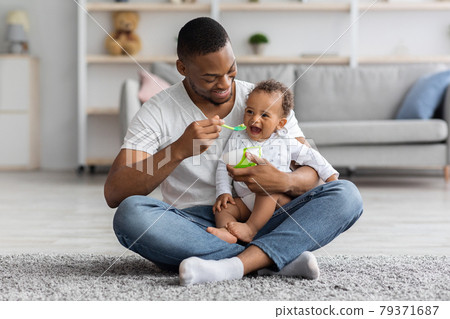 Happy Young Black Dad Spoon Feeding His Adorable Baby Son At Home 79371687