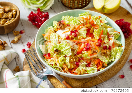 Dietary salad fresh vegetable of Chinese cabbage, carrots, apple, nuts and pomegranate with vinaigrette dressing on a white wooden table. 79372405