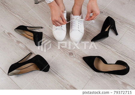 A woman chooses sports shoes instead of high-heeled shoes. Sneakers or shoes 79372715