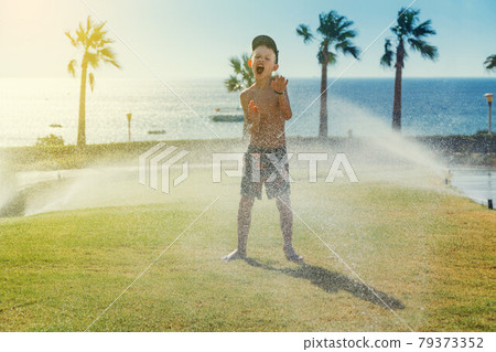 Happy boy playing with sprinklers near sea 79373352