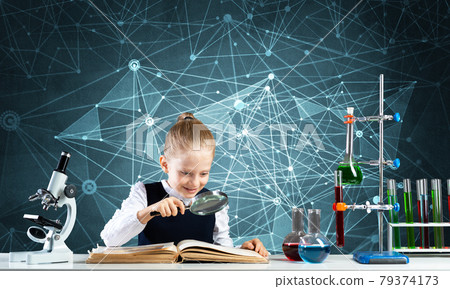 Little girl sitting at desk with magnifier 79374173