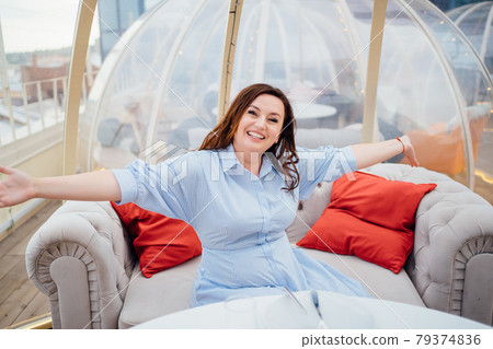 woman in a blue dress sits at tables in a cafe in the shape of a igloo on roof. woman in a blue dress sits at tables in a cafe in the shape of a igloo on roof. 79374836
