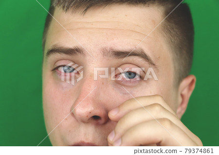 Tears in eyes of crying adult man. Green background. Chromakey 79374861