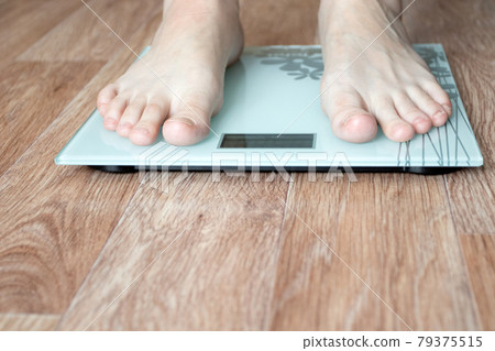 Female feet stepping on floor weigh scales. Female feet stepping on floor weigh scales. 79375515