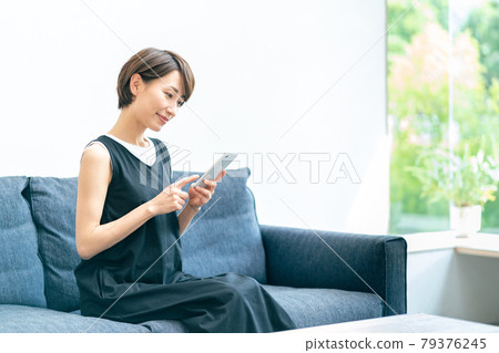 A middle-aged woman who uses her smartphone while relaxing in the living room. A middle-aged woman who uses her smartphone while relaxing in the living room. 79376245