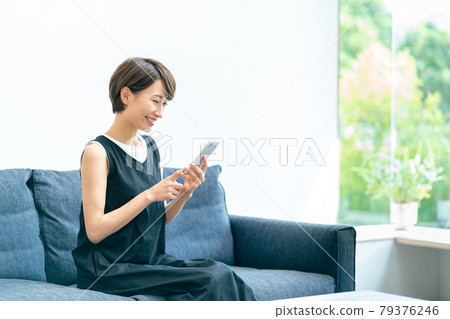 A middle-aged woman who uses her smartphone while relaxing in the living room. A middle-aged woman who uses her smartphone while relaxing in the living room. 79376246