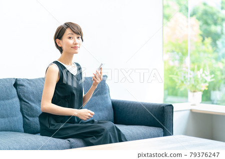 A middle-aged woman who uses her smartphone while relaxing in the living room. A middle-aged woman who uses her smartphone while relaxing in the living room. 79376247