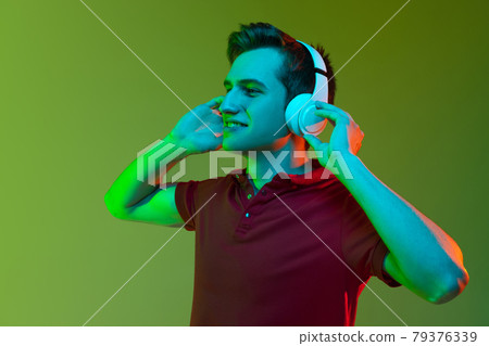 Portrait of young caucasian man in headphones isolated on green background in neon light Portrait of young caucasian man in headphones isolated on green background in neon light 79376339
