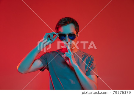 One young handsome caucasian guy in sunglasses isolated on red neon background. Concept of human emotions, facial expression. 79376379