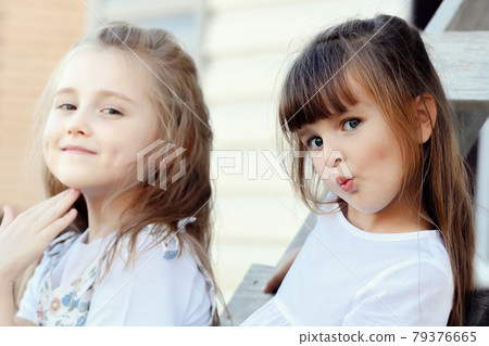 Two beautiful girls girlfriends sit on a summer day on a wooden staircase and look into the camera Two beautiful girls girlfriends sit on a summer day on a wooden staircase and look into the camera 79376665