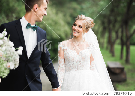 Romantic, fairytale, happy newlywed couple hugging and kissing in a park, trees in background Romantic, fairytale, happy newlywed couple hugging and kissing in a park, trees in background 79376710