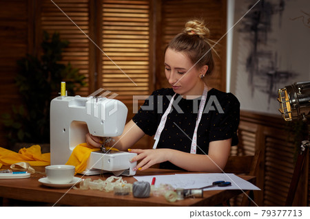 Beautiful young seamstress working on sewing machine Beautiful young seamstress working on sewing machine 79377713