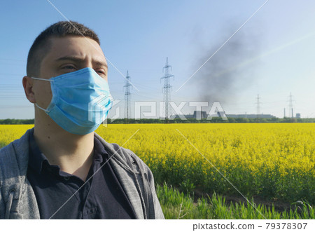 A man in a medical mask against the background of the plant. The concept of environmental pollution, ecology A man in a medical mask against the background of the plant. The concept of environmental pollution, ecology 79378307