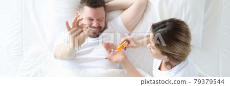 Woman giving man pill in bed top view Woman giving man pill in bed top view 79379544
