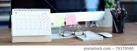 Loose leaf paper calendar standing near computer on desktop closeup Loose leaf paper calendar standing near computer on desktop closeup 79379560