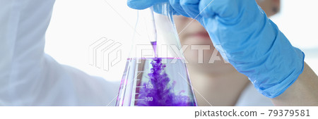 Woman scientist dripping purple liquid into flask with solvent closeup Woman scientist dripping purple liquid into flask with solvent closeup 79379581