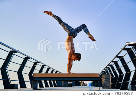 Fit man doing a hand stand while practicing yoga alone near the ocean against sky at dusk or dawn Fit man doing a hand stand while practicing yoga alone near the ocean against sky at dusk or dawn 79379597