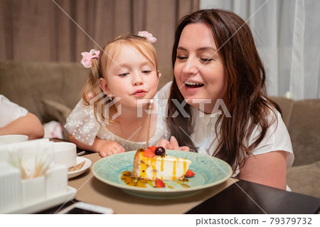 mom and daughter light and blow candle on piece of festive cake mom and daughter light and blow candle on piece of festive cake 79379732