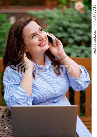 happy woman sits on an terrace and works on a laptop and talks on the phone happy woman sits on an terrace and works on a laptop and talks on the phone 79379735