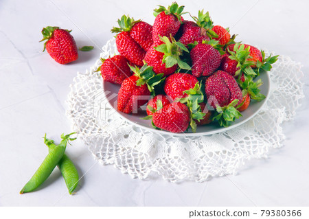 Fresh red strawberries and pods of green peas on white marble table. Fresh red strawberries and pods of green peas on white marble table. 79380366