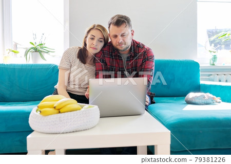 Serious middle-aged couple husband and wife with laptop sitting at home on couch 79381226