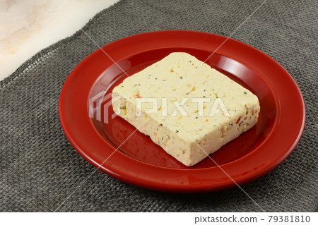 Block of tomato and basil feta cheese on red plate on gray burlap table runner 79381810