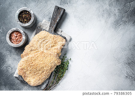 Wiener Raw schnitzel in breadcrumbs on wooden board. White background. Top view. Copy space Wiener Raw schnitzel in breadcrumbs on wooden board. White background. Top view. Copy space 79386305