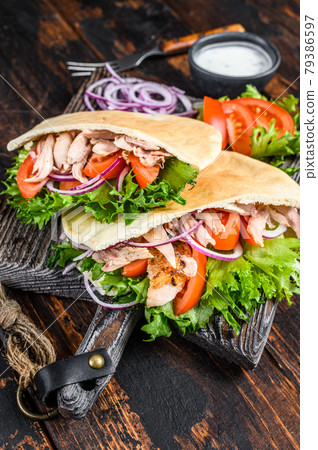 Greek gyros wrapped in pita breads with vegetables and sauce. Dark wooden background. Top view Greek gyros wrapped in pita breads with vegetables and sauce. Dark wooden background. Top view 79386597
