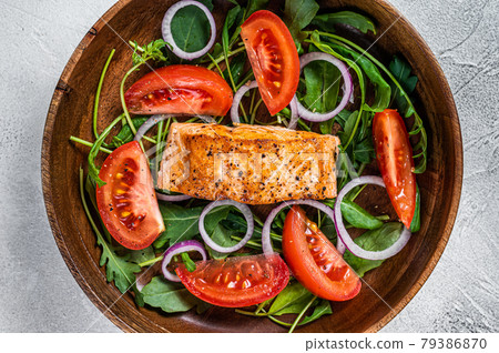 Salmon fillet steak salad with green leaves arugula, avocado and tomato in a wooden plate. White background. Top view 79386870