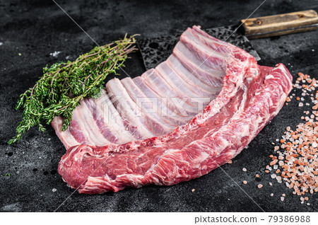 Raw rack of lamb ribs on butcher cutting board with herbs. Black background. Top view 79386988