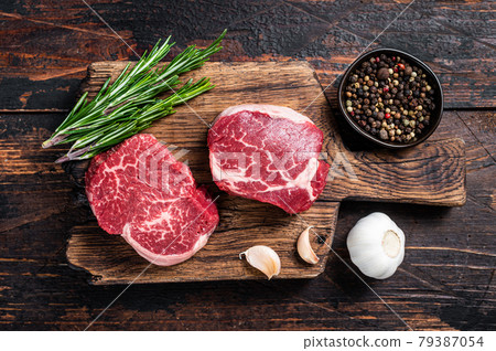 Fresh Raw Fillet Mignon tenderloin steaks on butcher cutting board with meat cleaver. Dark wooden background. Top view 79387054